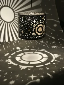 Lámpara colgante Planetario cilíndrica de metal calado con proyección de estrellas, planetas y un sol diseñada por Nico Berreta.